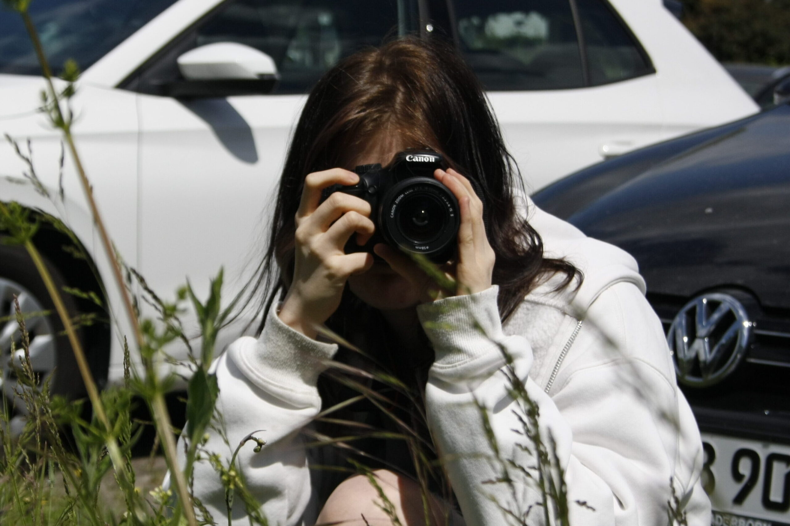 Bild von Mediendesignerin Angelina Rubow auf dem sie eine Kamera in der Hand vor ihrem Gesicht hat und in der Hocke ein Foto schießt.